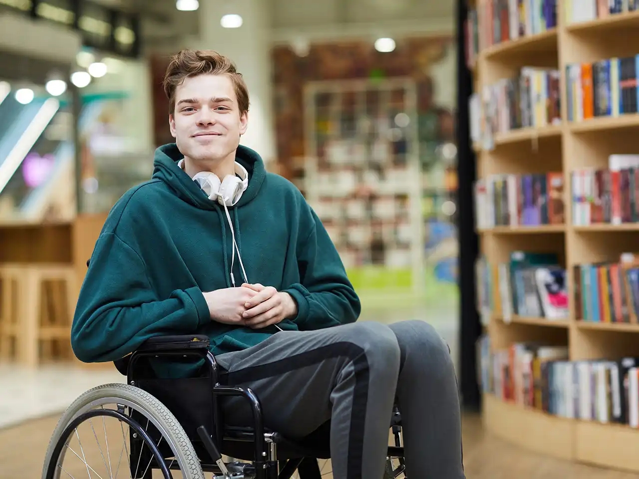 Junger Mann im Rollstuhl in der Bibliothek